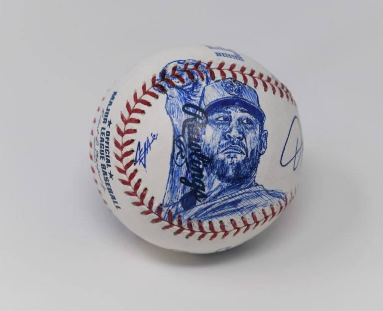 Jacob deGrom pitching sketched on a baseball with the artist's signature to the left of the sketch