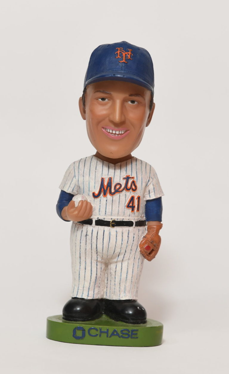 Bobblehead figurine of Tom Seaver in white Mets jersey and blue cap standing on green platform that reads 