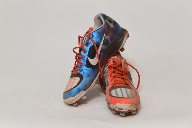 Blue cleat propped up on a red one, both with wear